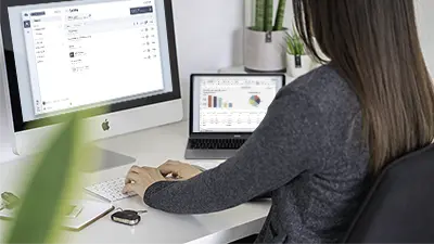 Kvinne som sitter og arbeider en PC der skjermen viser Infoskjermens brukergrensesnitt.