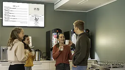 Tre elever i prat ved infoskjerm i skolekantine