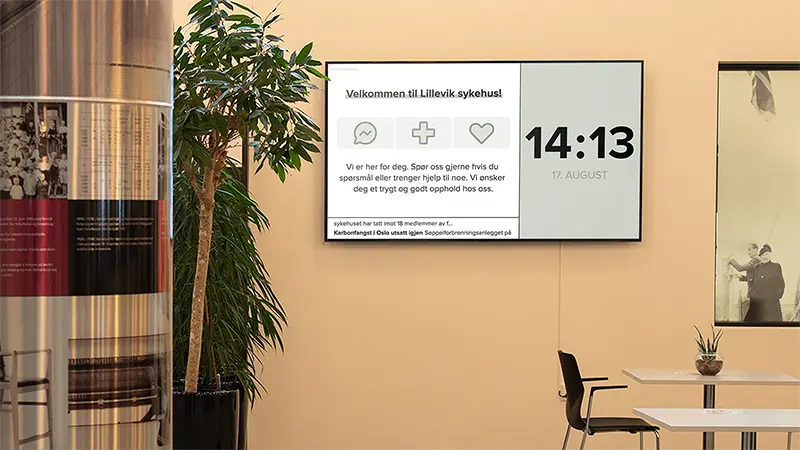 En infoskjerm i en ventesone på et sykehus viser en velkomst-melding, klokke og nyheter.Foto.